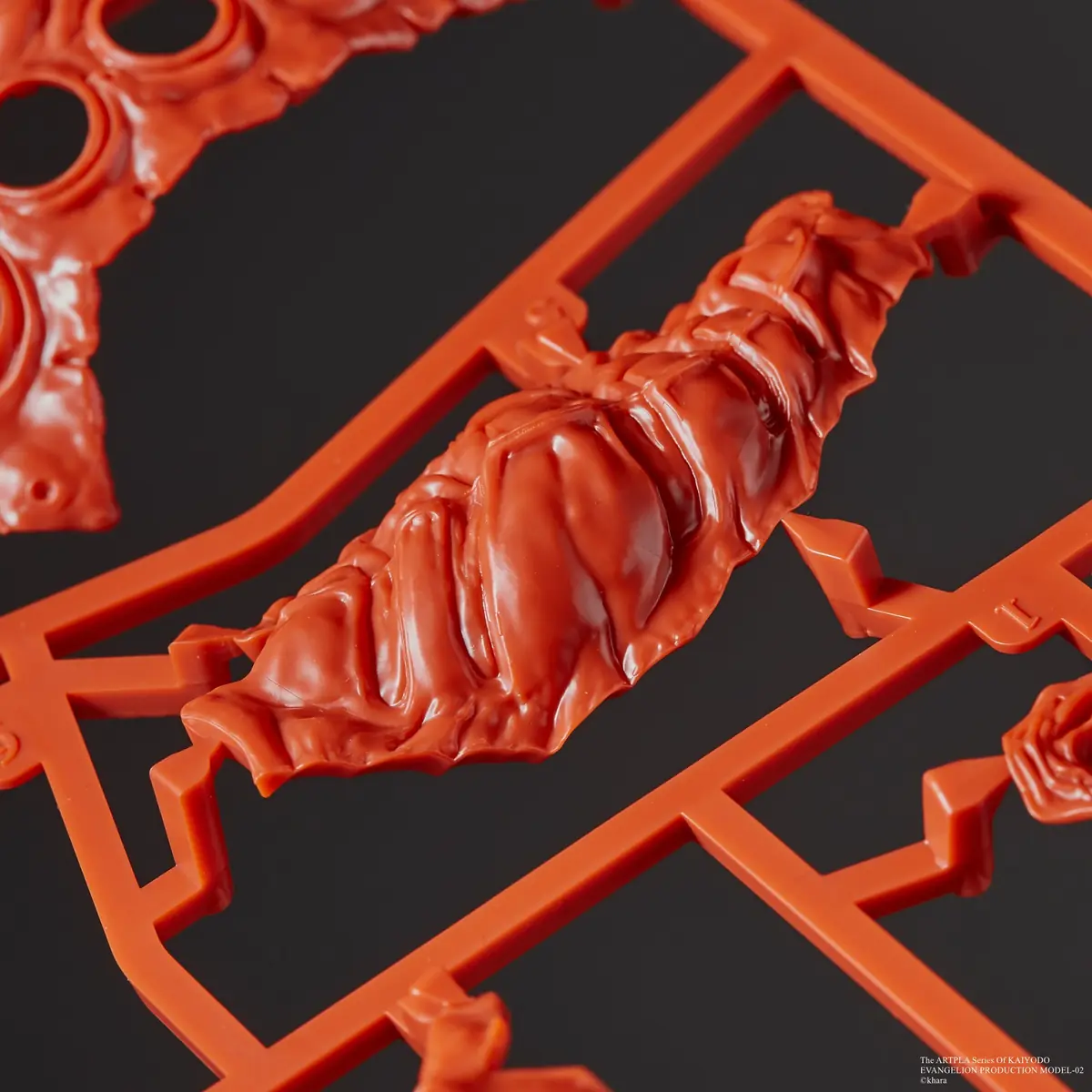 Close-up of a layered sculpted red part attached to a plastic runner