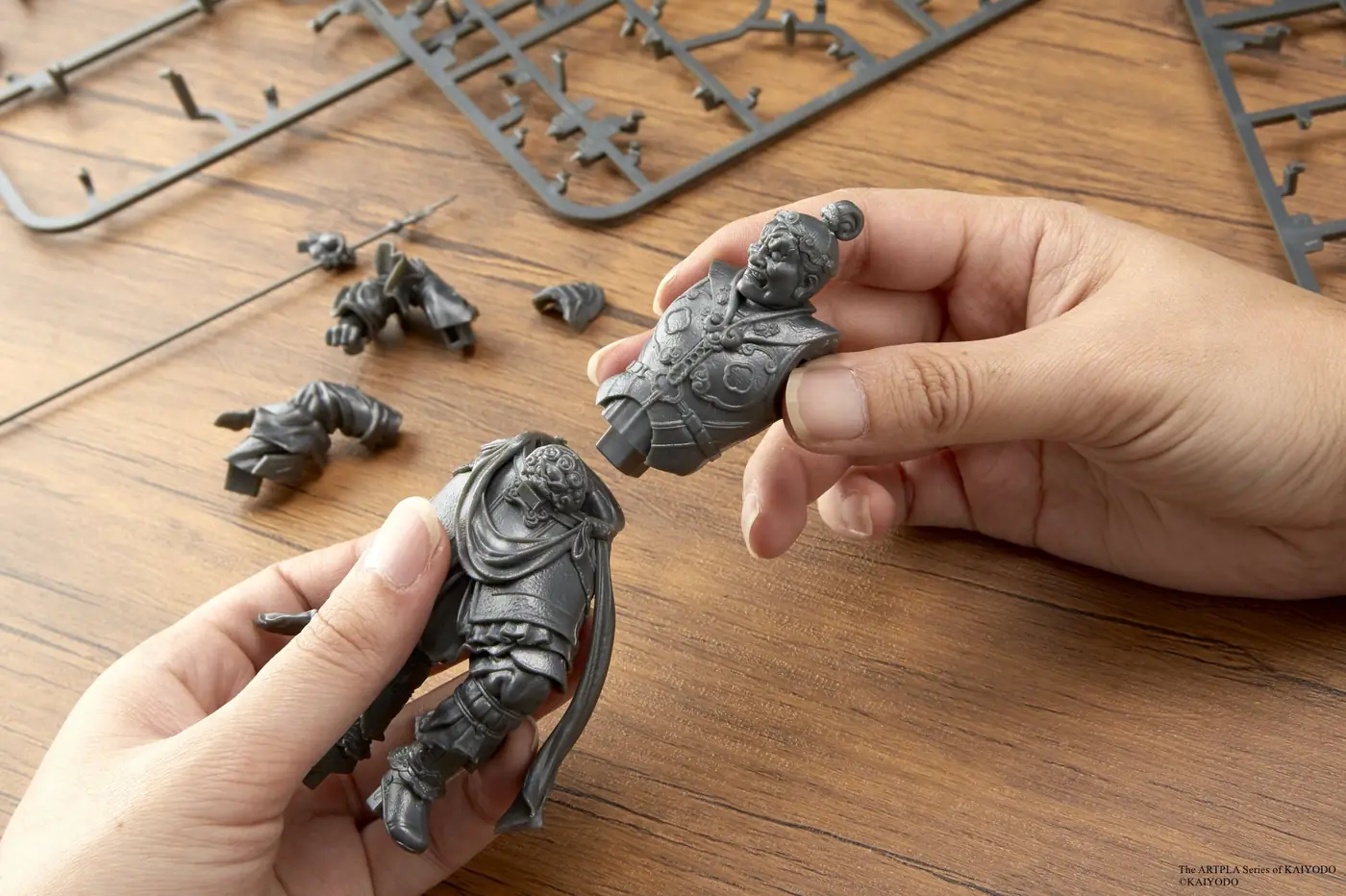 Hands joining an armored figure's upper body to its lower-body assembly on a worktable
