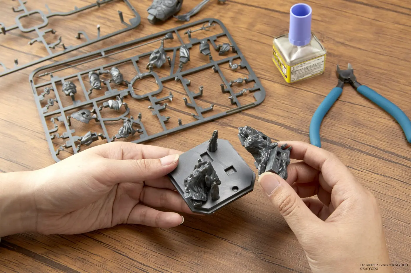 Hands fitting gray scenic parts onto an octagonal display base beside model runners and tools