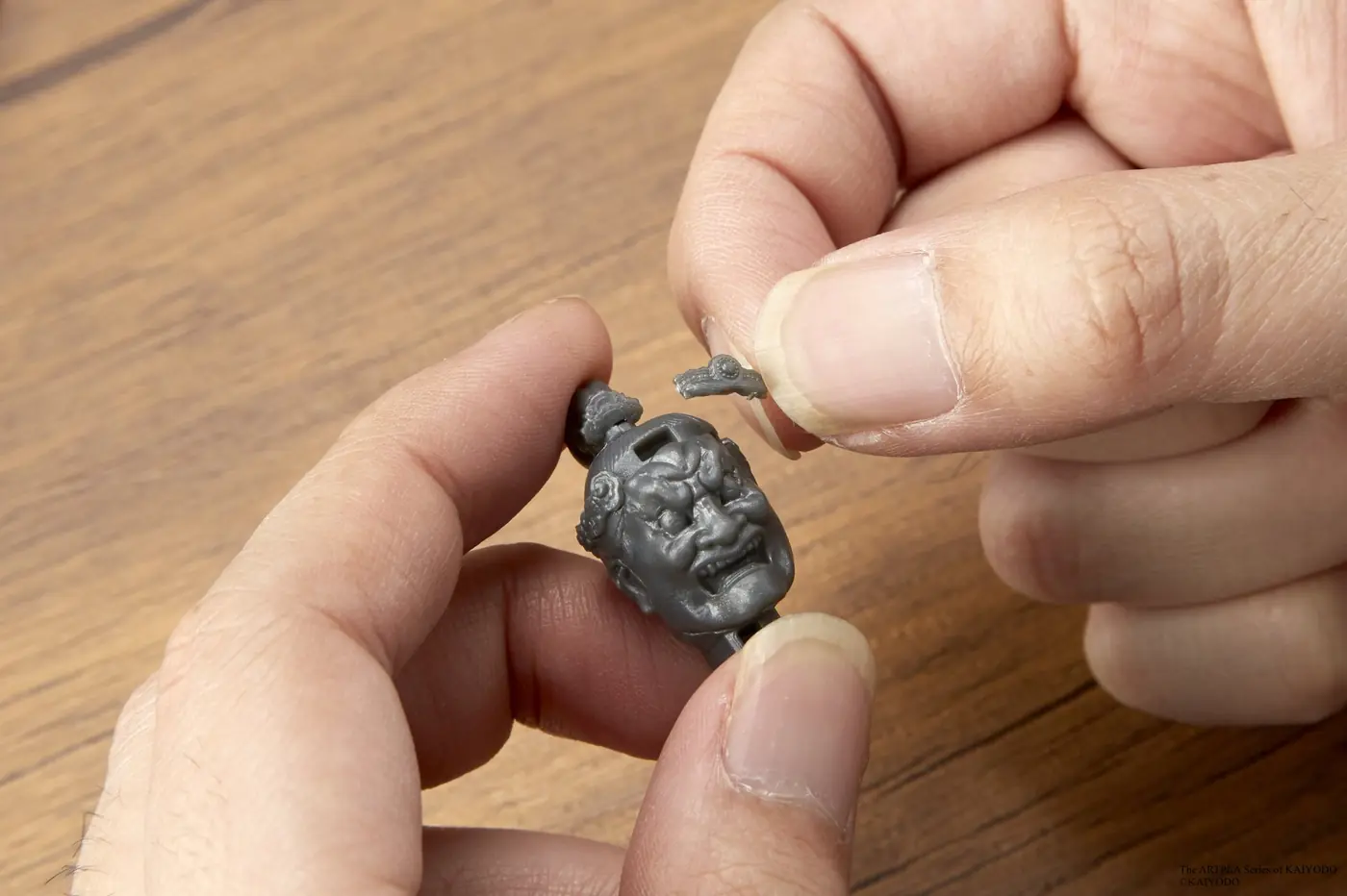 Close-up of hands attaching a small ornament to a gray sculpted model head