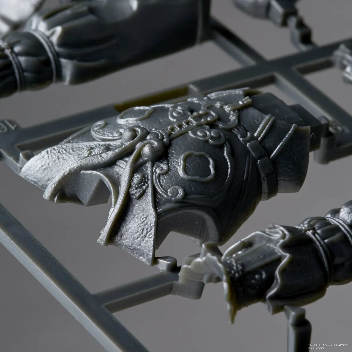 Macro view of an ornate gray armor panel still attached to a plastic runner