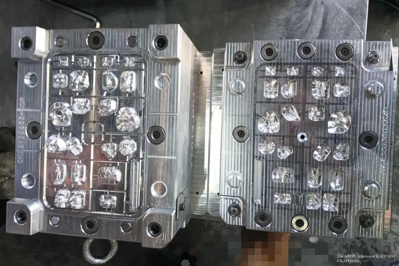 Open metal mold with many small component cavities photographed on a workshop surface
