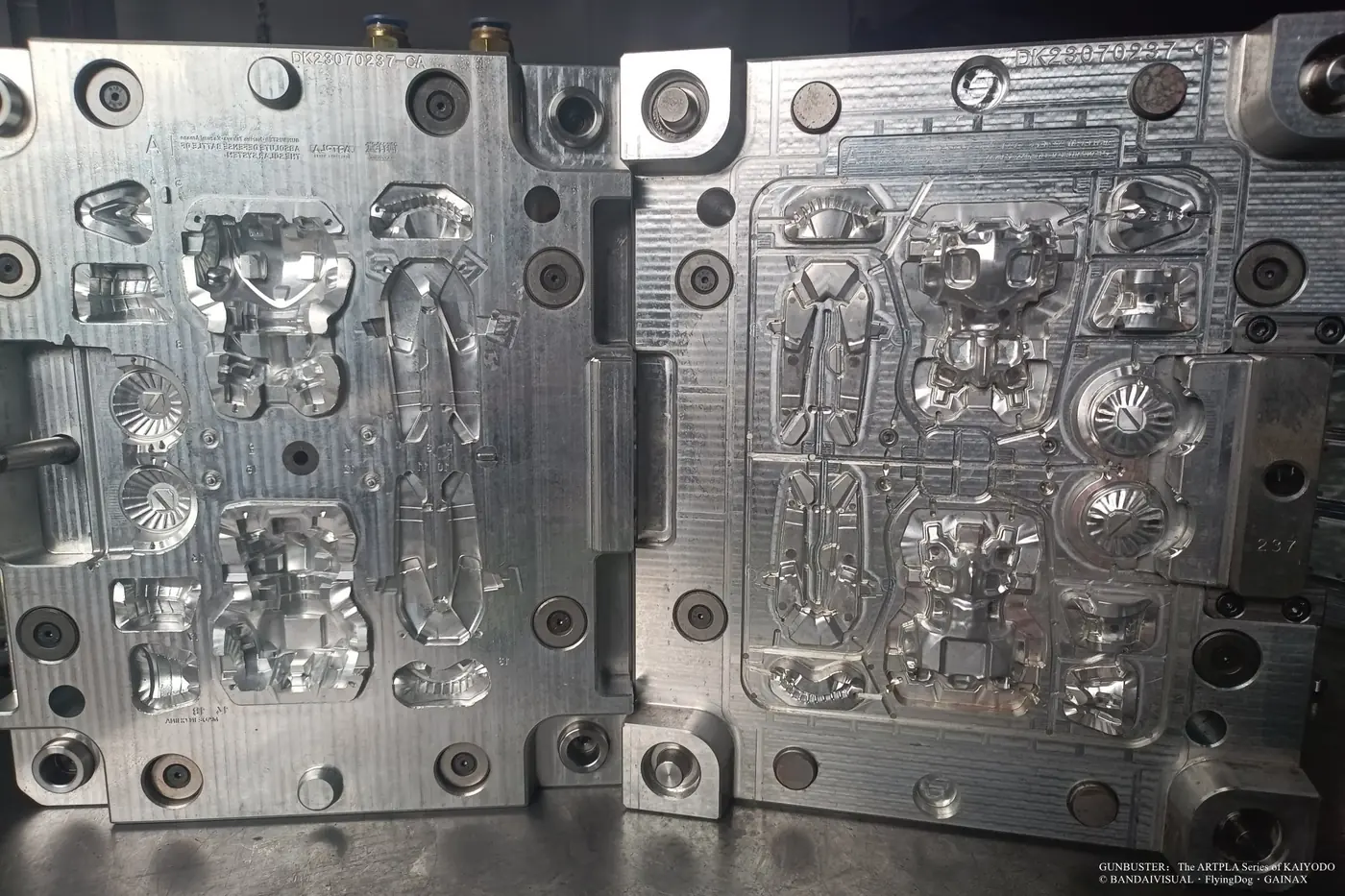 Open metal mold with large robot body panels, circular components and smaller mechanical parts