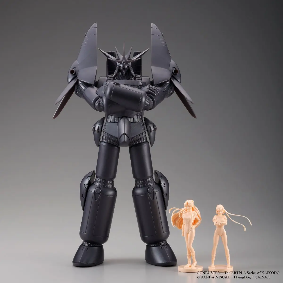 Front studio view of the dark Gunbuster model with arms crossed beside two pale-orange character figures