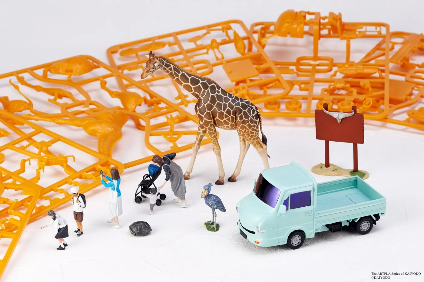 Painted giraffe, miniature people, birds, tortoise, sign and pale blue truck staged in front of orange plastic runners